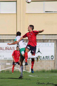 El futbolista Borja Fernández saltando por un balón mientras defiende la camiseta del CD Barco